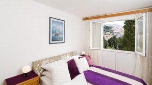 Un dormitorio con cama, mesita de noche, ventana con vistas a un pueblo y un cuadro en la pared.
