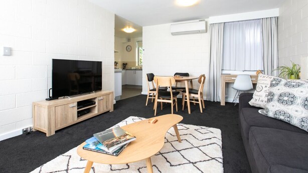 A modern living room with a flat-screen TV, a wooden coffee table, a sofa, and a dining area with chairs.