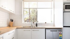 A modern kitchen with white cabinets, a wooden countertop, a built-in dishwasher, and a window with a view of trees.