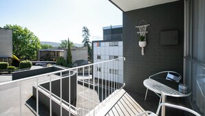 A balcony with a metal railing, a small table with a chair, and a hanging plant.
