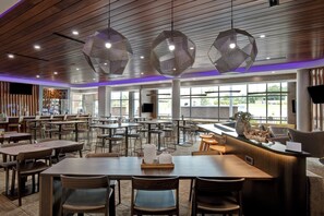 Un vaste espace dédié à la restauration, avec de nombreuses tables et chaises, un comptoir d’accueil et de grandes fenêtres qui laissent entrer la lumière naturelle.