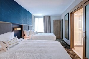 Habitación de hotel con dos camas, un ventanal grande con cortinas, zona de ducha y diseño moderno con patrón geométrico en la pared.