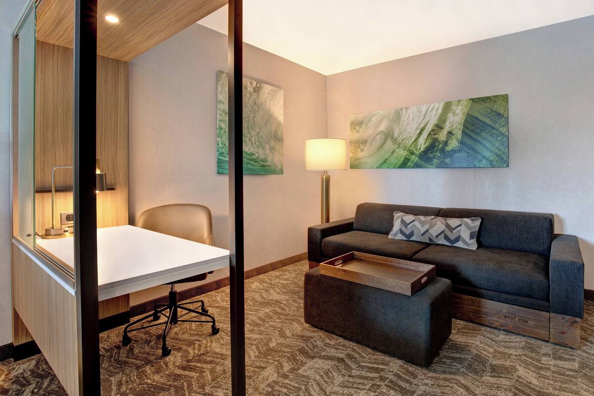 Ein modernes Hotelzimmer mit Schreibtisch, einer Couch, einer Lampe und abstrakter Wandkunst.