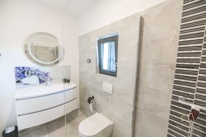 A modern bathroom with a white vanity, a round mirror, a toilet, and a shower area.