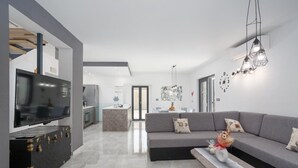 Een moderne woonkamer met een grijze bank, een televisie en een keuken op de achtergrond.