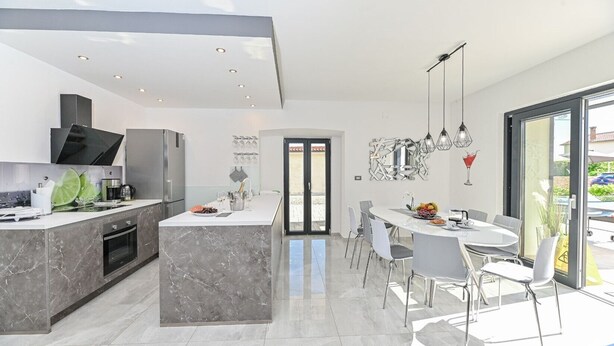 Een moderne keuken met een marmeren eiland, roestvrijstalen apparatuur en een eethoek met een glazen tafel en stoelen.