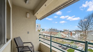A balcony with a view of a residential street, a chair, and a small table.