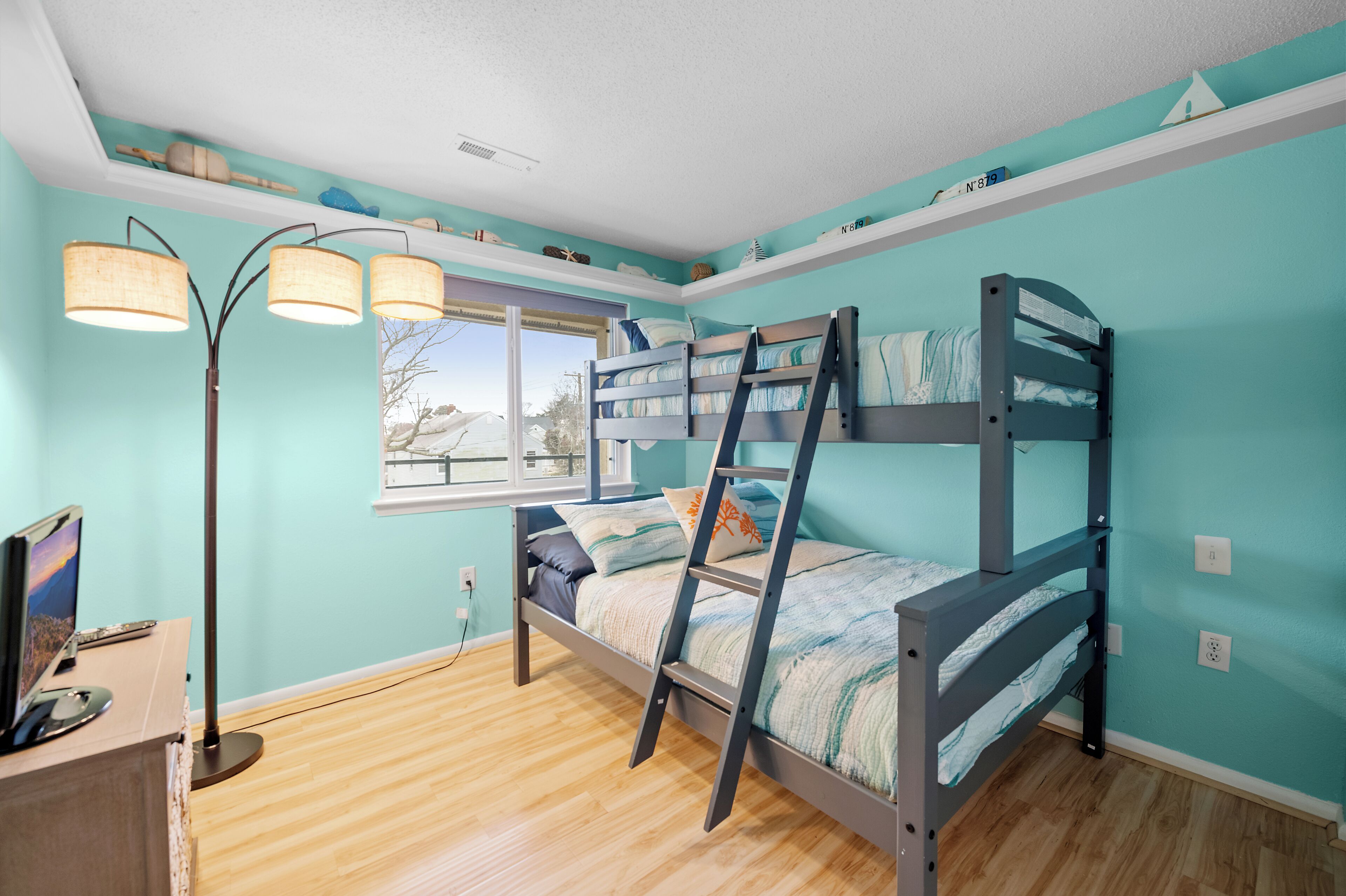 Une chambre avec un lit superposé, une fenêtre, un bureau avec un ordinateur et une lampe sur pied.