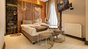 Ein modernes Hotelzimmer mit einem großen Bett, einem runden Esstisch, zwei Barhocker, einem an der Wand montierten Fernseher und einer Marmor-Akzentwand.