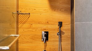 Zona de ducha con paneles de madera, un cabezal de ducha de mano y un grifo empotrado.