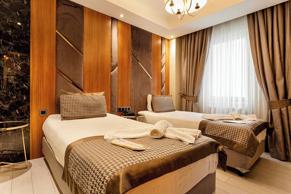 Habitación de hotel con dos camas, paneles de madera, detalles de mármol y un amplio ventanal con cortinas.