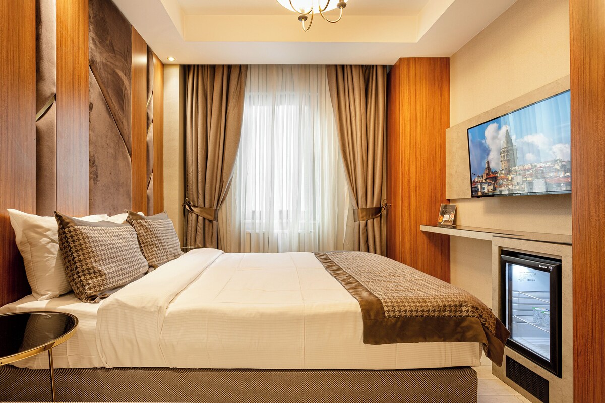 Habitación de hotel con una cama grande, un televisor montado en la pared y una ventana con cortinas.