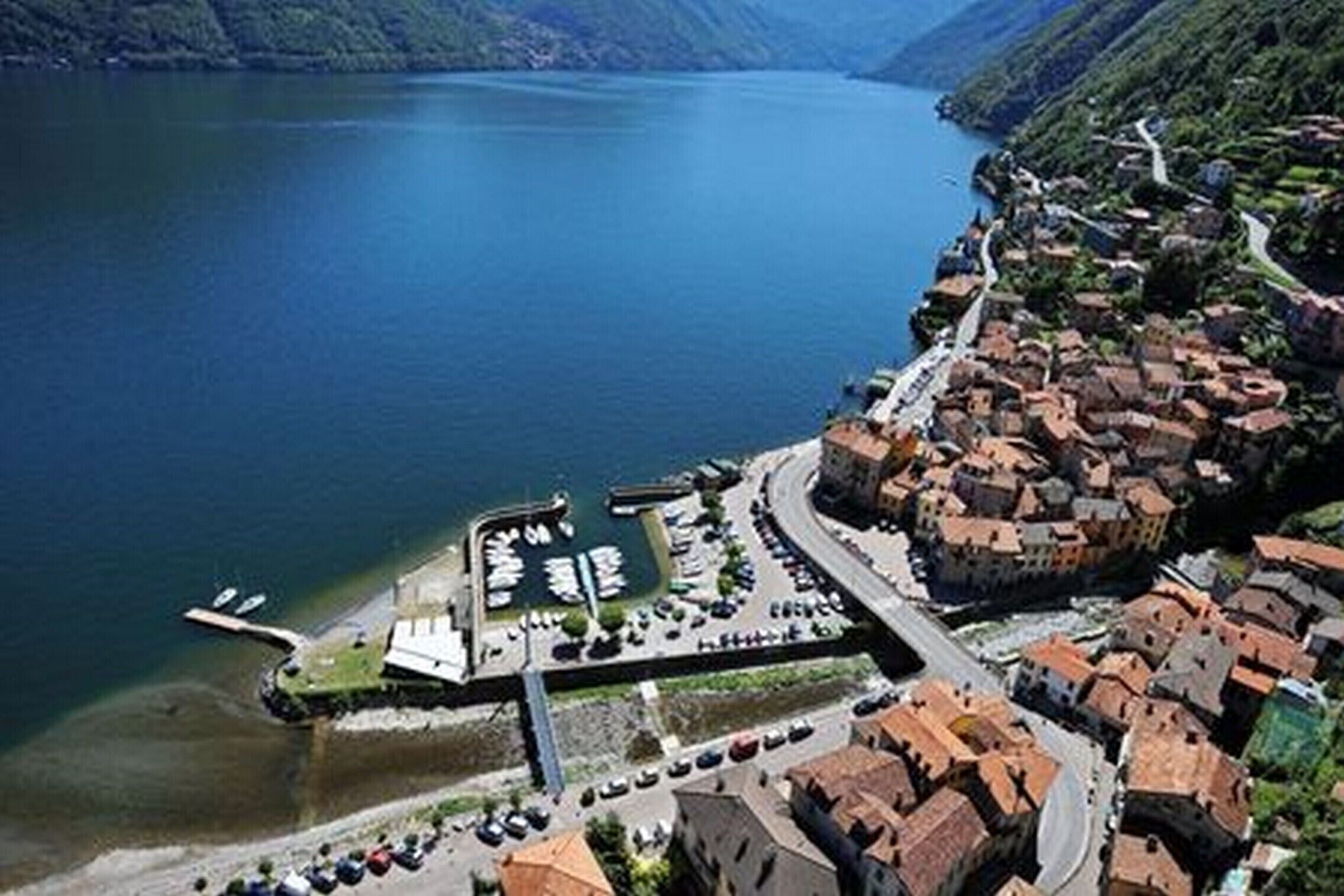 An aerial view of a lakeside village with a marina, narrow roads, and traditional buildings.