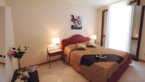 Habitación de hotel con una cama grande, dos mesitas de noche con lámparas, un florero con flores y un cuadro en la pared.