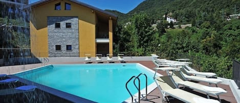 A swimming pool with lounge chairs and a building with a stone facade.