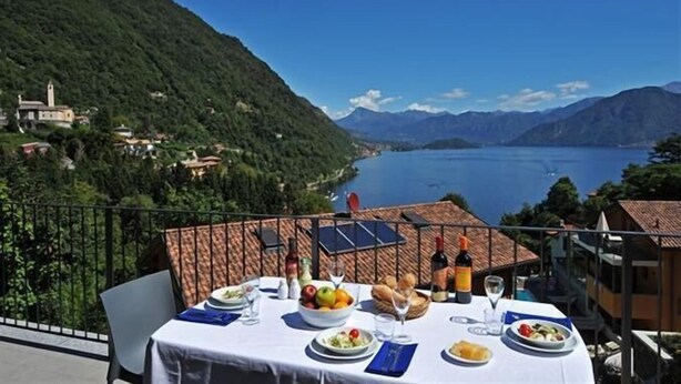 Una mesa servida con comida y bebidas en un balcón con vistas a un lago y montañas.