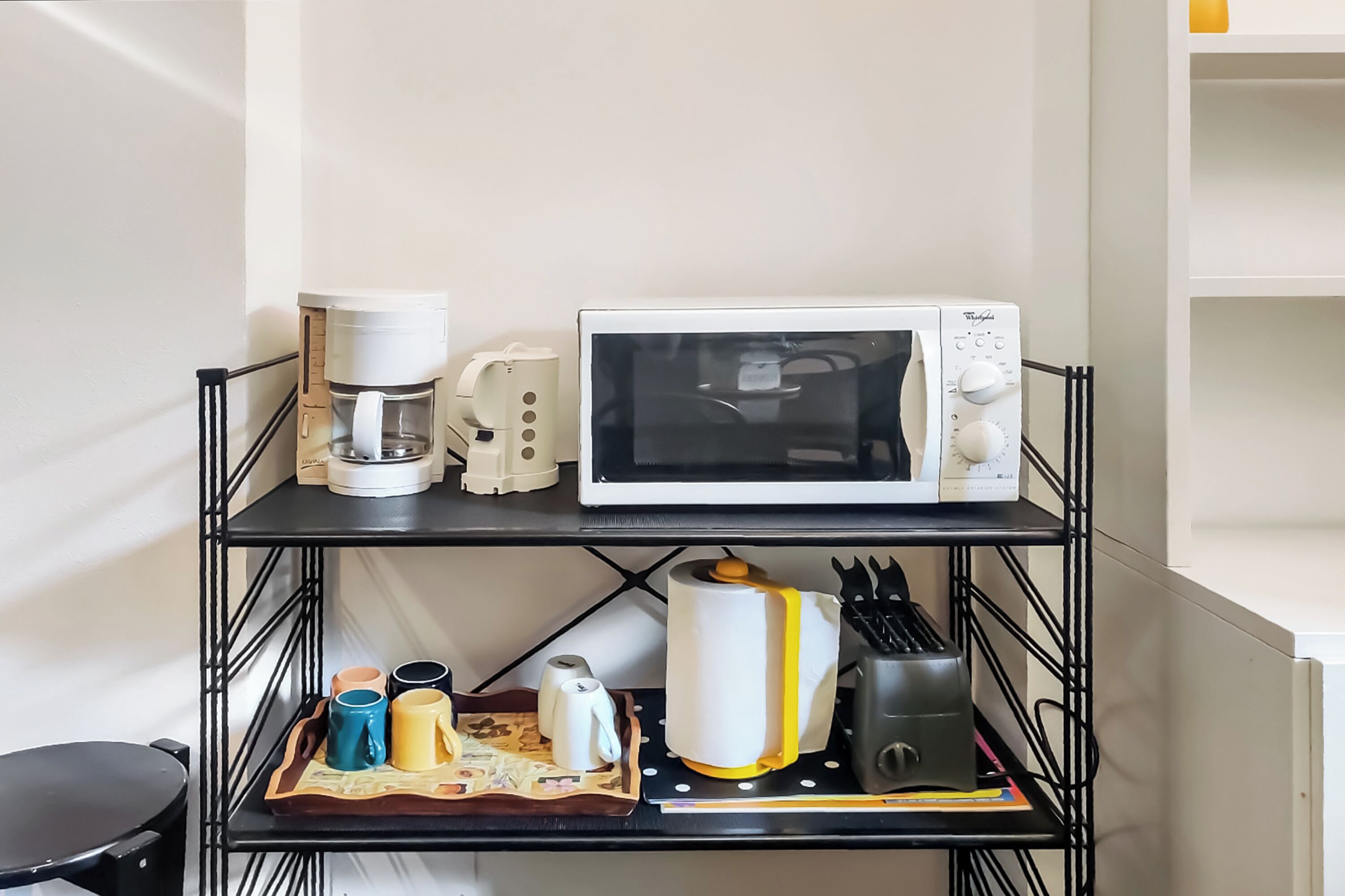 Una cocina equipada con microondas, cafetera y una bandeja con tazas y utensilios.