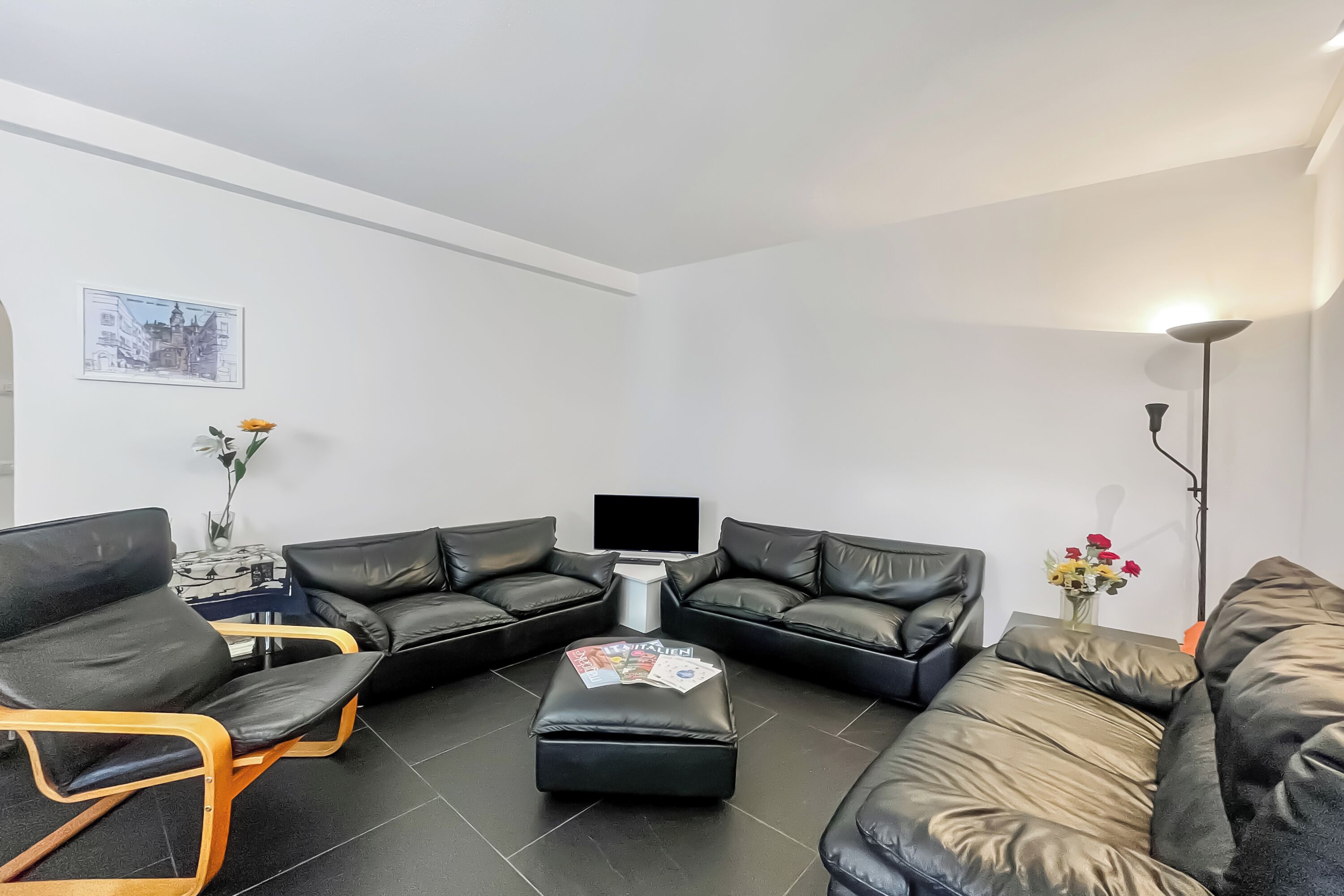 Ein modernes Wohnzimmer mit einem Ecksofa, einem Stuhl mit Holzrahmen, einem kleinen Beistelltisch und einem Flachbildfernseher.