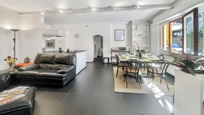 A modern living room with a leather sofa, a dining area with a table and chairs, and a kitchen in the background. - Menaggio 57 (Menaggio)