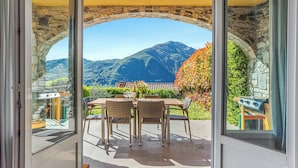 A patio with a stone archway, wicker furniture, and a view of mountains. - Villa Tremezzo (Tremezzina)