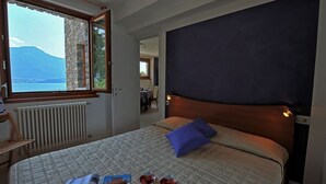 A hotel room with a large bed, a view of a mountain through a window, and a dining area visible in the background. - Gera Panoramica (Gera Lario)