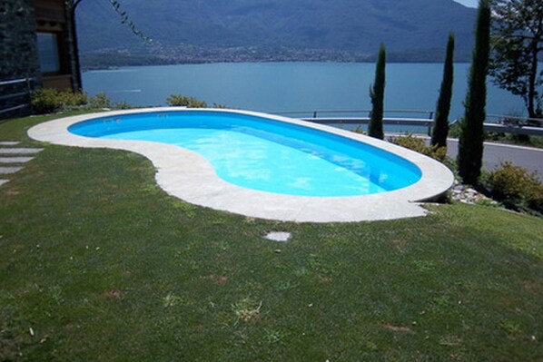 Una piscina de borde curvo, rodeada de césped cuidado y con vistas a un lago y montañas al fondo.