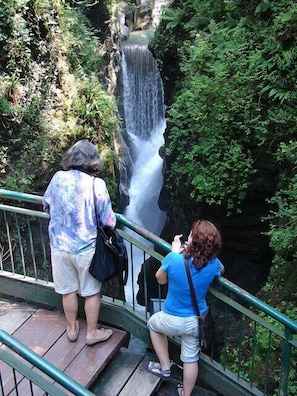 Dos personas contemplando una cascada desde una plataforma de madera con barandilla metálica.