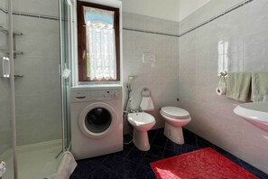 A bathroom with a washing machine, two toilets, a shower, and a sink.