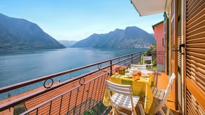 A balcony with a table set for two, overlooking a lake with mountains in the background. - Bella Lake View (Colonno)