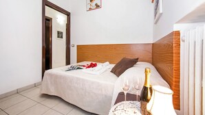 A neatly made bed with a wooden headboard, a bedside table with a bottle and glasses, and a framed picture on the wall. - Bella Lake View (Colonno)
