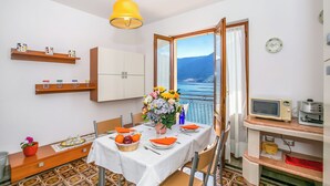 A dining area with a table set for two, a vase of flowers, and a view of the sea through an open window. - Bella Lake View (Colonno)