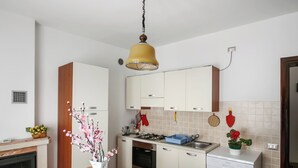 A modern kitchen with white cabinets, a gas stove, a dishwasher, and a dining area with a table set for two. - Bella Lake View (Colonno)