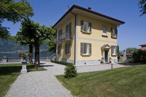 A two-story yellow building with balconies, a gravel pathway, and a grassy lawn. - Villa Chic (Lezzeno)