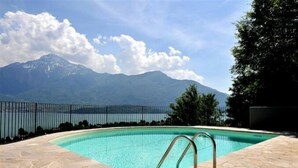 A swimming pool with a metal ladder, surrounded by stone tiles, and a mountain view in the background. - Residenza Vercana Giardino (Vercana)