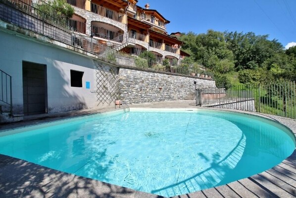 A swimming pool with a stone wall and a wooden deck. - Residenza Vercana Giardino (Vercana)