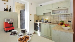 A kitchen with a coffee machine, a sink, cabinets, and a countertop with fruits and pastries. - Residenza Vercana Giardino (Vercana)