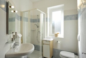 A bathroom with a glass-enclosed shower, a sink, a toilet, and a window. - Residenza Vercana Giardino (Vercana)