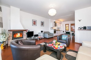 A modern living room with a fireplace, leather sofas, a coffee table with magazines, and a kitchen in the background. - Bellavista Grande (Menaggio)