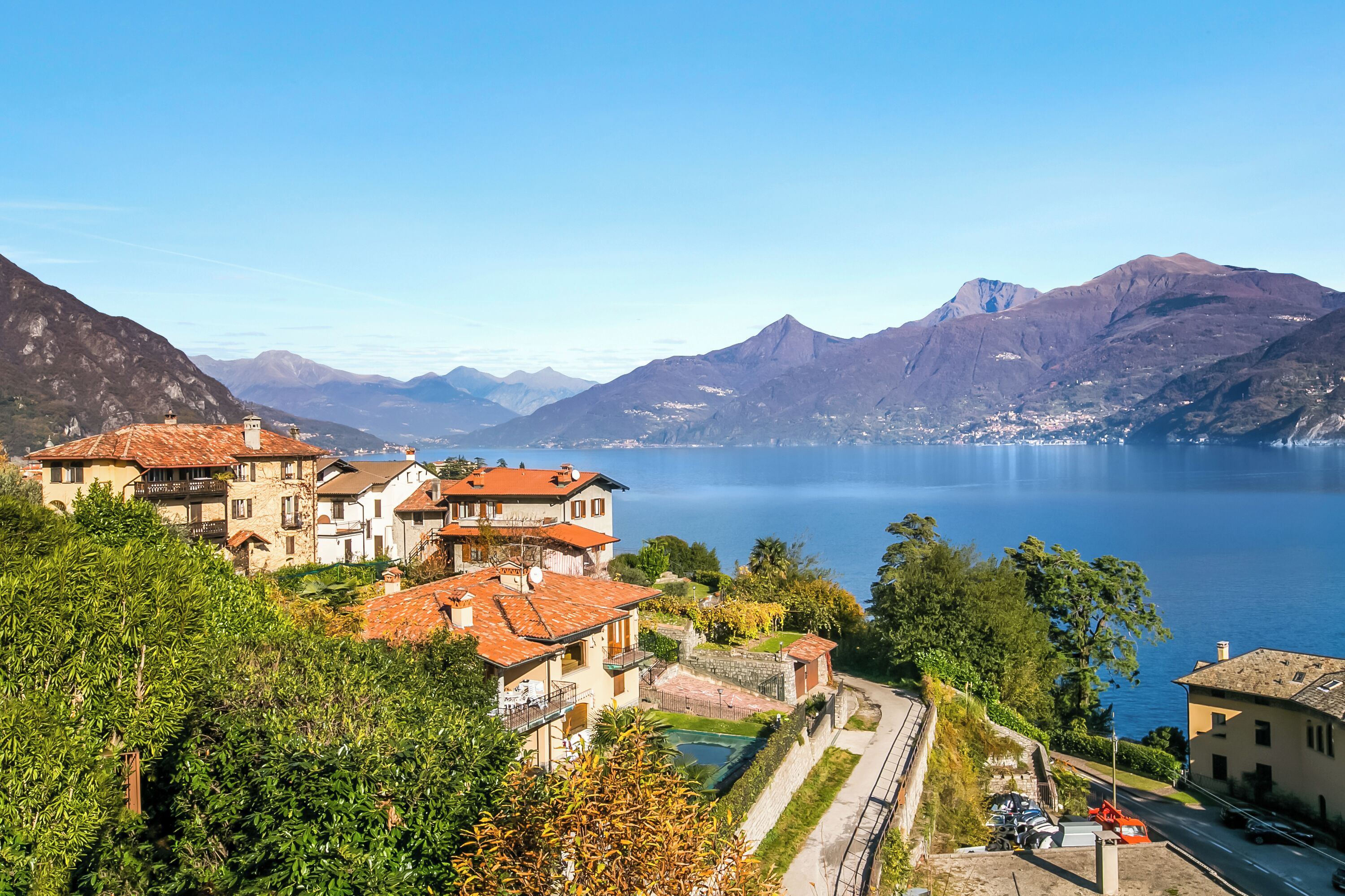 A coastal town with traditional buildings, a clear view of the sea, and mountains in the background.