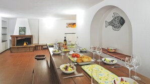 A dining area with a long wooden table set for a meal, a fireplace, and a wall-mounted fish artwork. - Bellavista Grande (Menaggio)