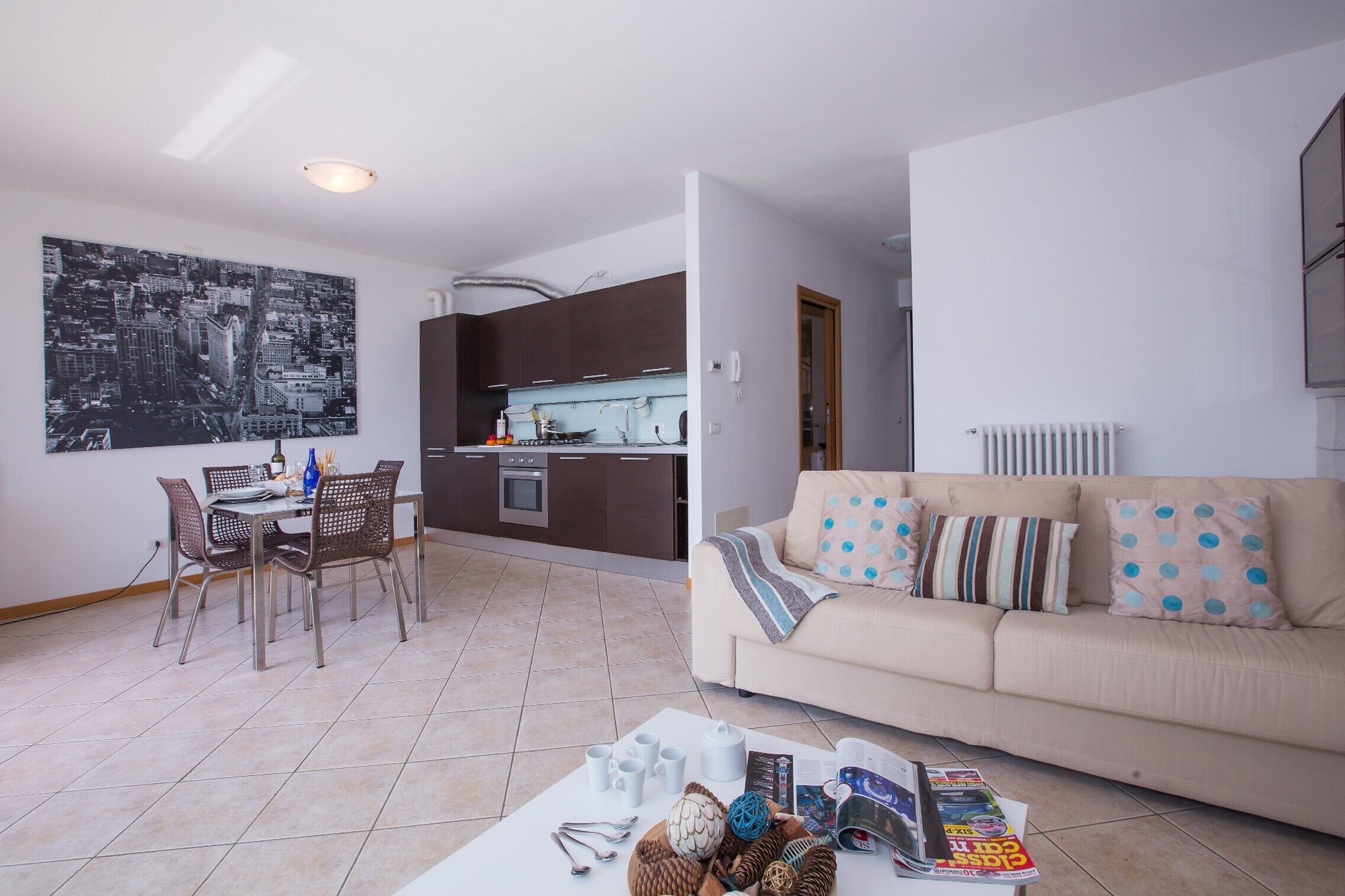 A modern living room with a beige sofa, a dining table with chairs, and a kitchen in the background.