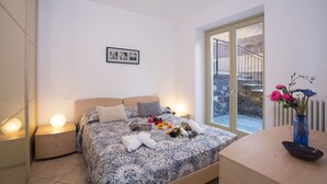 Un dormitorio con cama, lámparas de noche, un jarrón con flores y vista a una pared de piedra a través de una puerta de vidrio.