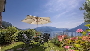 Un patio con una mesa, sillas, una sombrilla y vistas a montañas y un lago.
