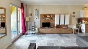 A modern living room with a large window, a flat-screen TV, a wooden cabinet, and a grey sofa.