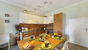 A modern kitchen with white cabinets, a wooden dining table set with breakfast items, and a white door in the background.