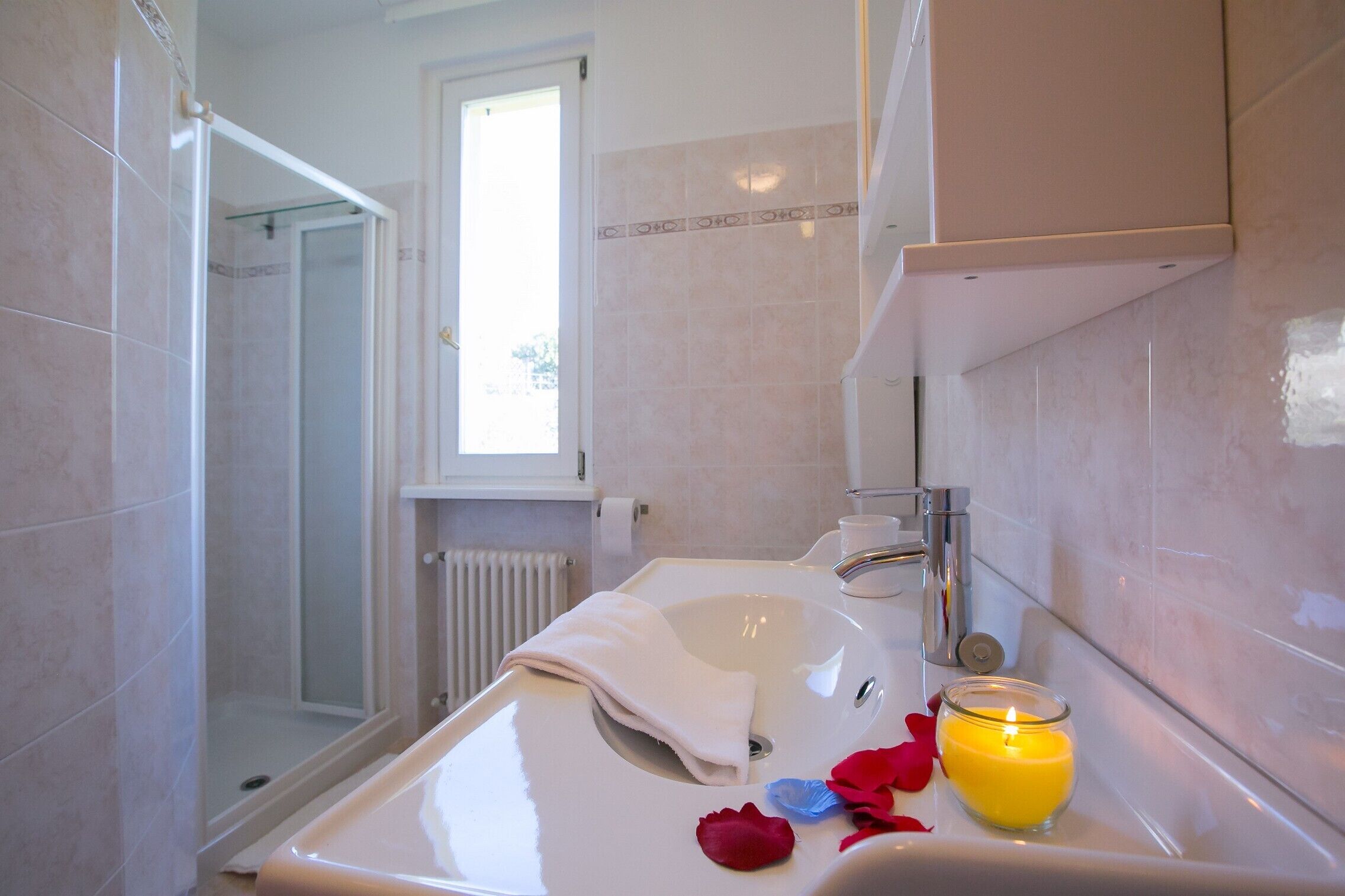 Un baño con lavamanos blanco, cabina de ducha de vidrio y ventana.