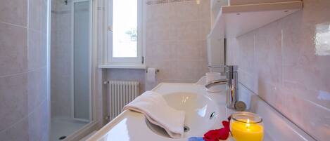 Un baño con lavamanos blanco, cabina de ducha de vidrio y ventana.