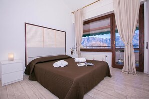 A hotel room with a bed, a nightstand, a window with curtains, and a view of mountains. - Cadenabbia Fantastico (Griante)