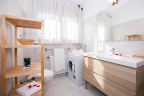 A modern bathroom with a wooden shelf, a washing machine, a sink, and a mirror.