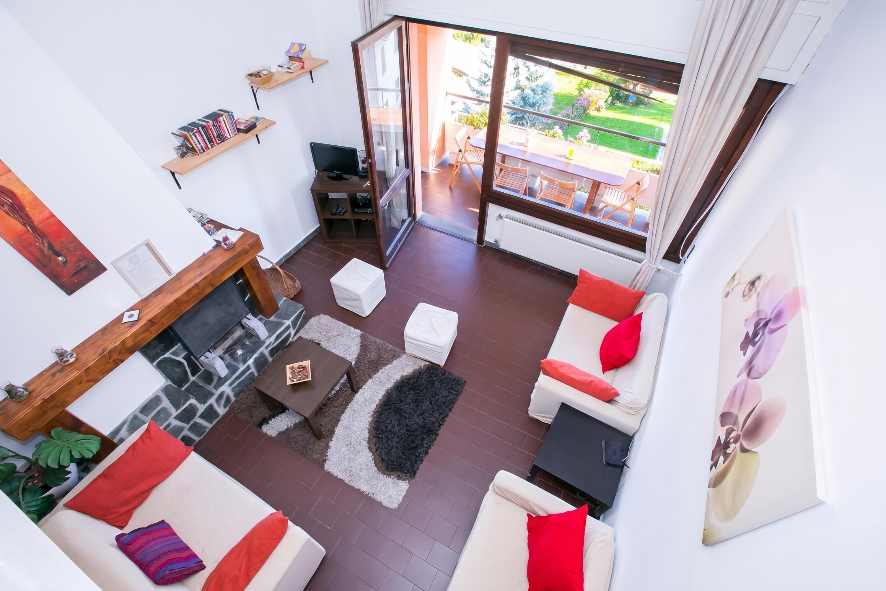 A living room with a fireplace, sofas, a coffee table, and a view of a garden through large windows.